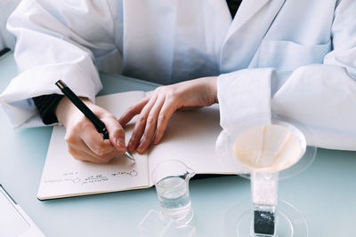 Young scientist writing chemical formula on book in laboratory