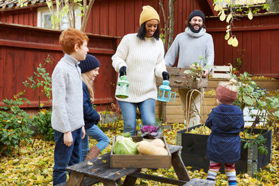 Male and female collecting fresh produce from garden while children standing in yard