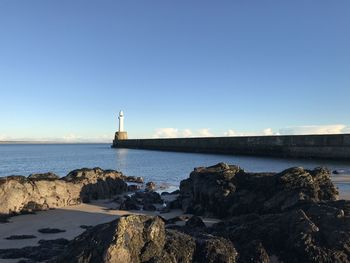 Lighthouse by sea against clear blue sky