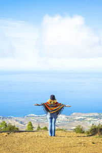 Rear view of woman standing at beach against sky