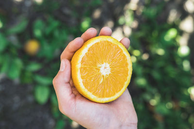 The boy is holding a half of a juicy orange in his hands.