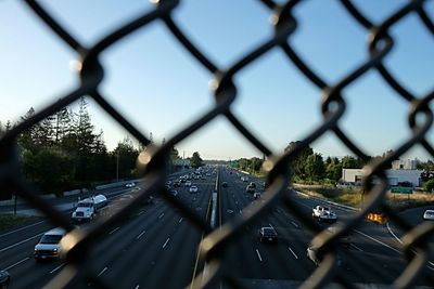 Close-up of cars on road seen through chainlink fence