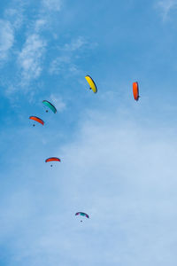 Low angle view of people paragliding against sky