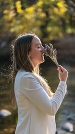 Side view of young woman blowing bubbles while standing outdoors