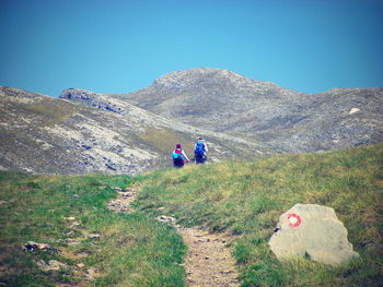 Rear view of men walking on mountain against clear blue sky