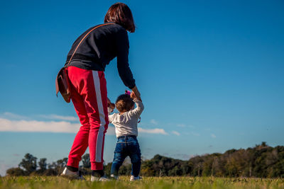 Low angle view of mother holding daughter walking on land against blue sky