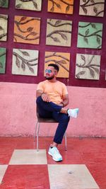 Young man sitting on chair against multi colored wall