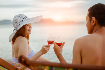 Low angle view of friends drinking glass against sea