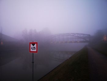 Road sign on bridge against sky at dusk