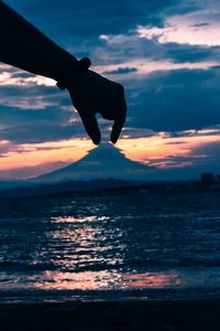 Silhouette person on sea against sky during sunset