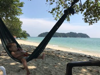 Man relaxing on beach against sky