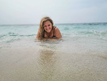 Portrait of smiling young woman at beach against sky