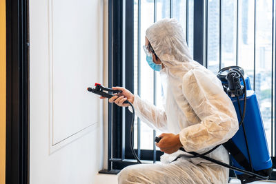 Man wearing protective suit sanitizing home