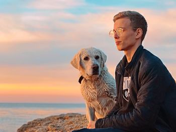 Man with dog at beach against sky during sunset