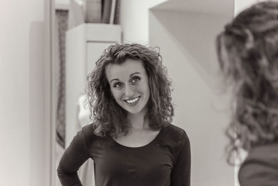 Smiling woman with curly hair viewing her reflection in a dressing room mirror