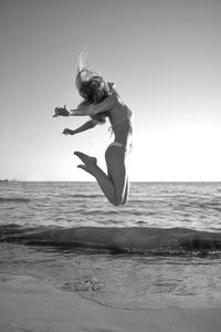 Woman jumping on beach against clear sky