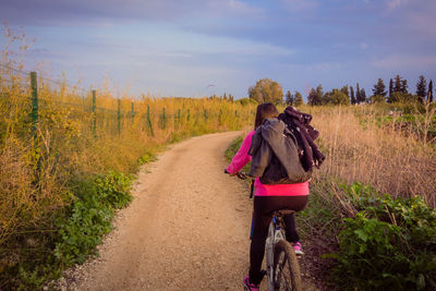 Rear view of woman walking on road amidst field