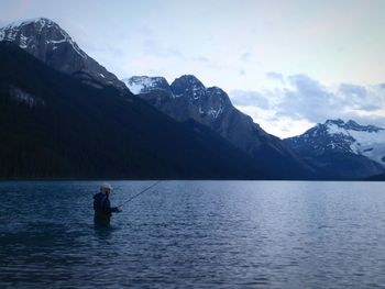 Scenic view of fishing by snowcapped mountains against sky