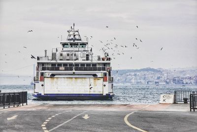 Birds flying over ship in sea against sky