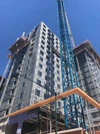 Low angle view of crane by building against sky