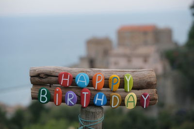 Happy birthday text composed with multi colored stone letters on wood with old village on the back 