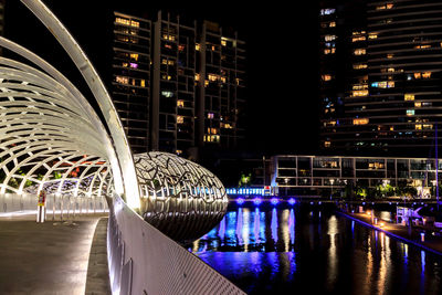 Illuminated bridge over river by buildings at night