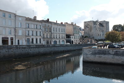 Buildings by canal against sky in city