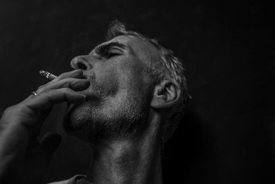 Close-up of man smoking cigarette against black background