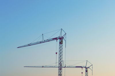 Low angle view of cranes against clear blue sky