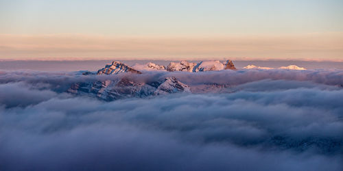 Idyllic shot of snowcapped mountain peaks amidst clouds against sky