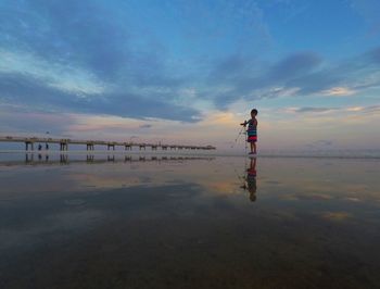 Rear view of woman standing on beach against sky during sunset