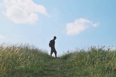 Silhouette man walking on grassy land against sky