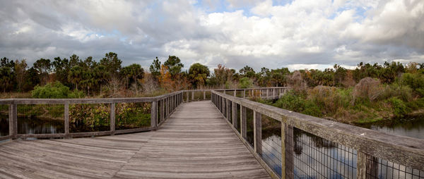 Panoramic shot of footbridge amidst trees against sky