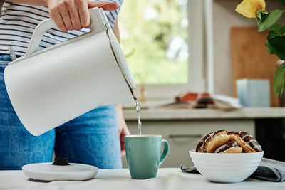 Woman pouring water from kettle for brewing tea