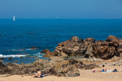 People on rocks by sea against sky