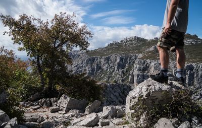 Low section of man standing on rock against sky