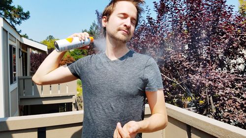 Young man holding ice cream standing against plants