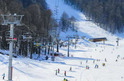 A chairlift with skiers and snowboarders. to  right of it is a gentle slope, where many beginners l