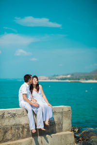 Full length of couple kissing on sea shore against blue sky