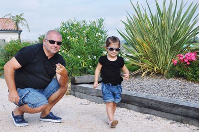 Smiling father looking at stylish daughter walking by plants in yard