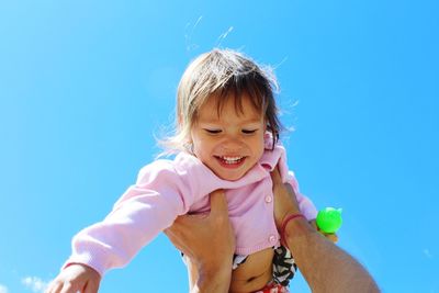 Cropped hands of man lifting daughter against clear blue sky