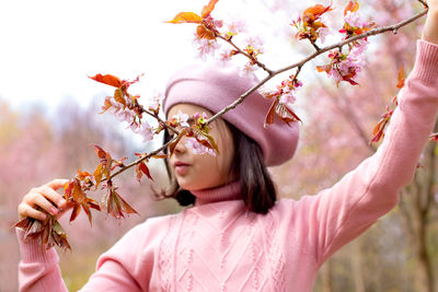 A little girl in a pink jumper hold a branch of cherry blossoms, in the park during the day