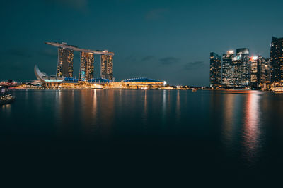 Illuminated city by sea against sky at night