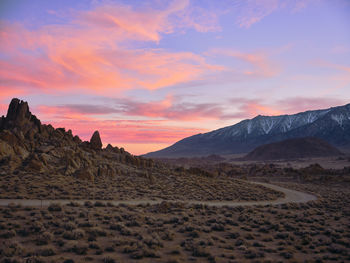 Sunset behind rock formations in an arid desert landscape.