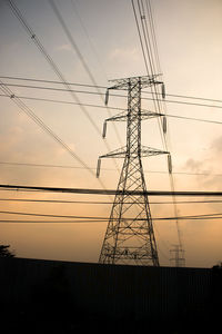 Low angle view of electricity pylon against sky at sunset