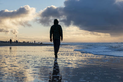 Rear view of man standing at beach during sunset