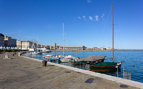 Sailboats moored at harbor against blue sky