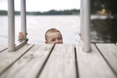 Portrait of happy boy climbing ladder of jetty against sky