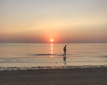 Silhouette man on beach against sky during sunset