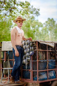 Full length of shirtless man sitting on wood